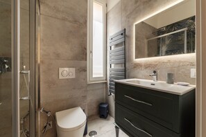 A modern bathroom with a glass shower enclosure, a toilet, a vanity with a mirror, and a towel rack.