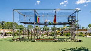 Ein Spielplatz mit einer Netz-Kletterkonstruktion, Schaukeln und einer Rutsche.