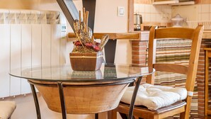 A dining area with a glass table, a wooden chair with a cushion, and a decorative plant centerpiece. - Apartment 'Tomillo' with Mountain View, Wi-Fi and Air Conditioning (Hinojares)