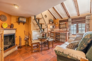 A cozy living room with a fireplace, a dining area with a table and chairs, and a kitchen area with a microwave. - Apartment 'Tomillo' with Mountain View, Wi-Fi and Air Conditioning (Hinojares)