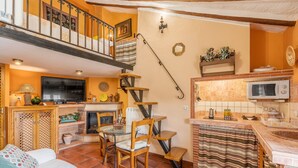 A cozy living room with a fireplace, a dining area, and a kitchen with a microwave. - Apartment 'Tomillo' with Mountain View, Wi-Fi and Air Conditioning (Hinojares)