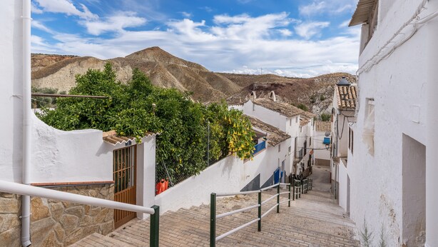 A narrow street with white buildings, a stone wall, and a mountain in the background. - Apartment 'Tomillo' with Mountain View, Wi-Fi and Air Conditioning (Hinojares)