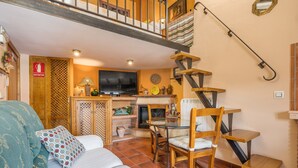 A cozy living room with a sofa, a TV, a fireplace, and a staircase. - Apartment 'Tomillo' with Mountain View, Wi-Fi and Air Conditioning (Hinojares)