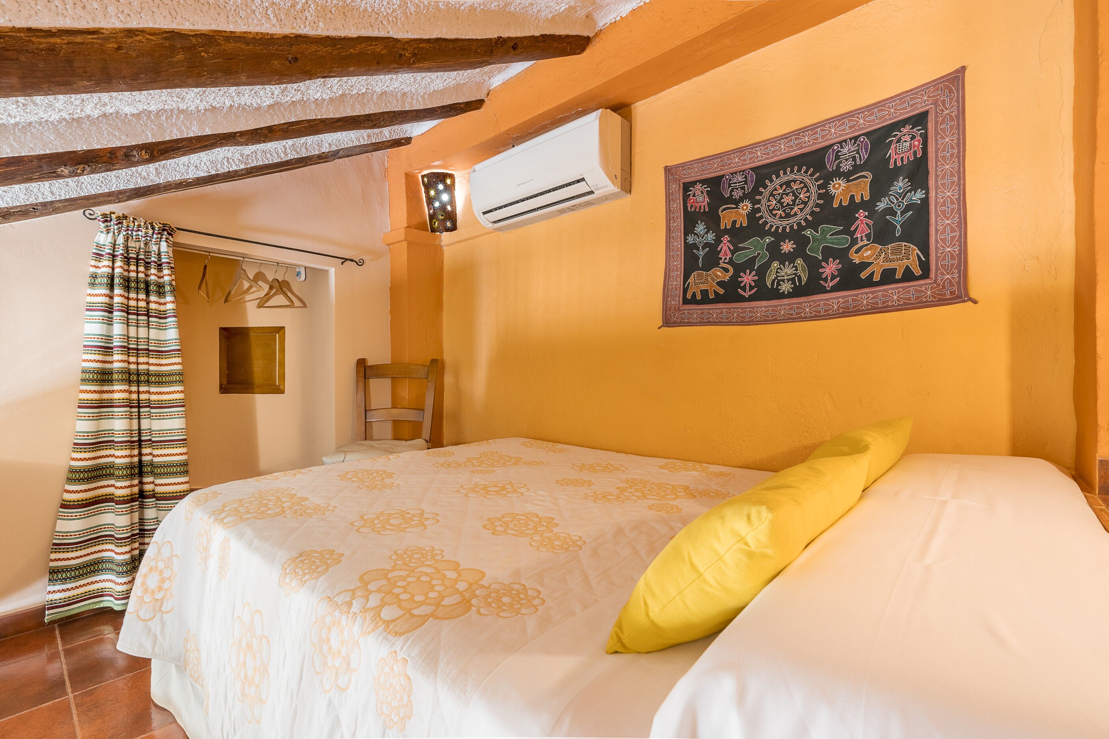 Una camera da letto con un letto, una lampada a sospensione, un condizionatore d'aria, un arazzo a parete e una porta con tenda a righe.