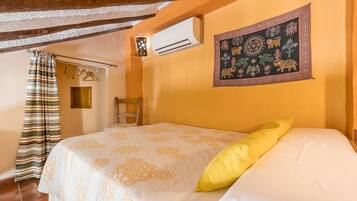 Una camera da letto con un letto, una lampada a sospensione, un condizionatore d'aria, un arazzo a parete e una porta con tenda a righe.