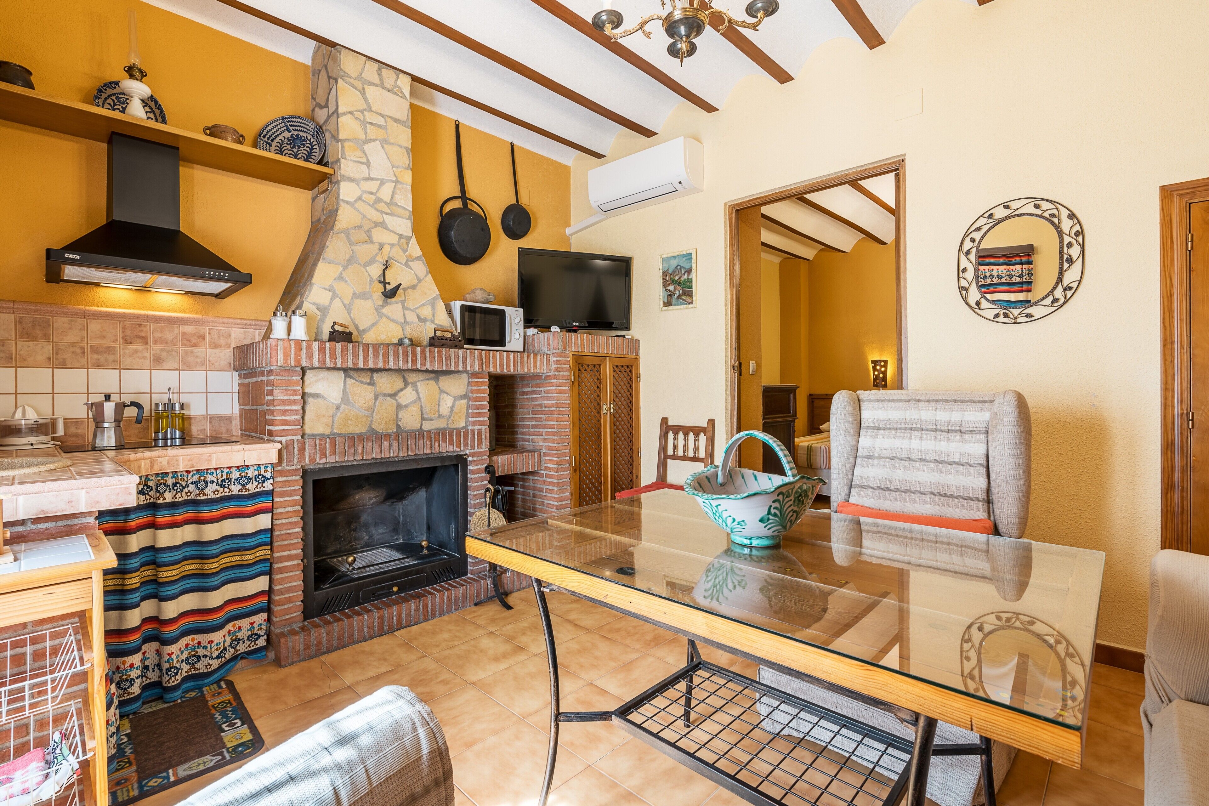 A kitchen with a stone fireplace, a TV, and a dining area with a glass table.