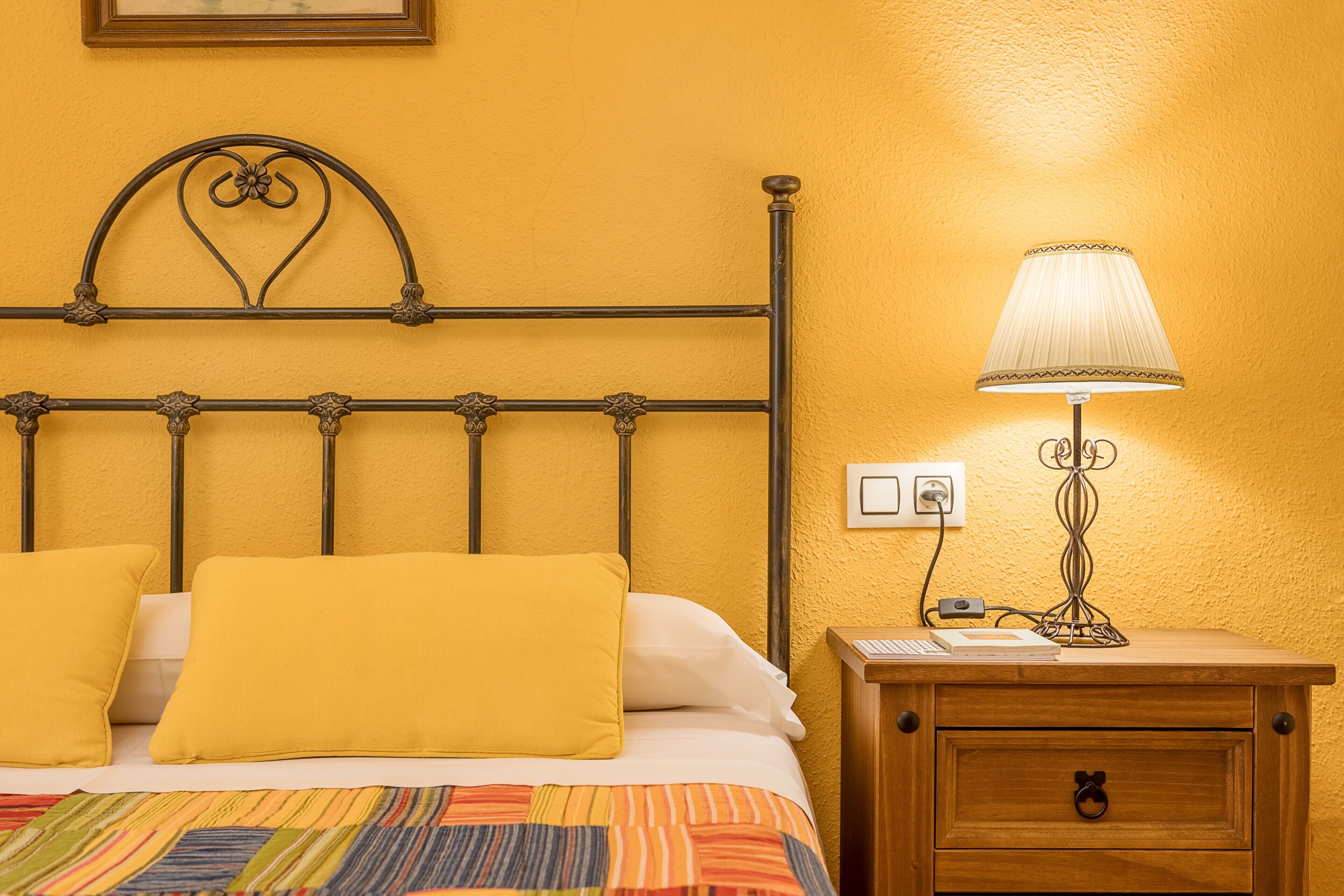 A bed with a metal headboard, a bedside table with a lamp, and a wooden nightstand.