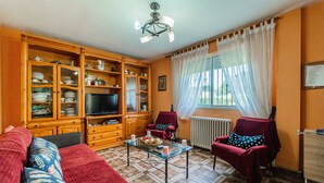 Un salon comprenant un canapé, des fauteuils, une table basse en verre, des meubles en bois, un téléviseur et une fenêtre avec des rideaux.