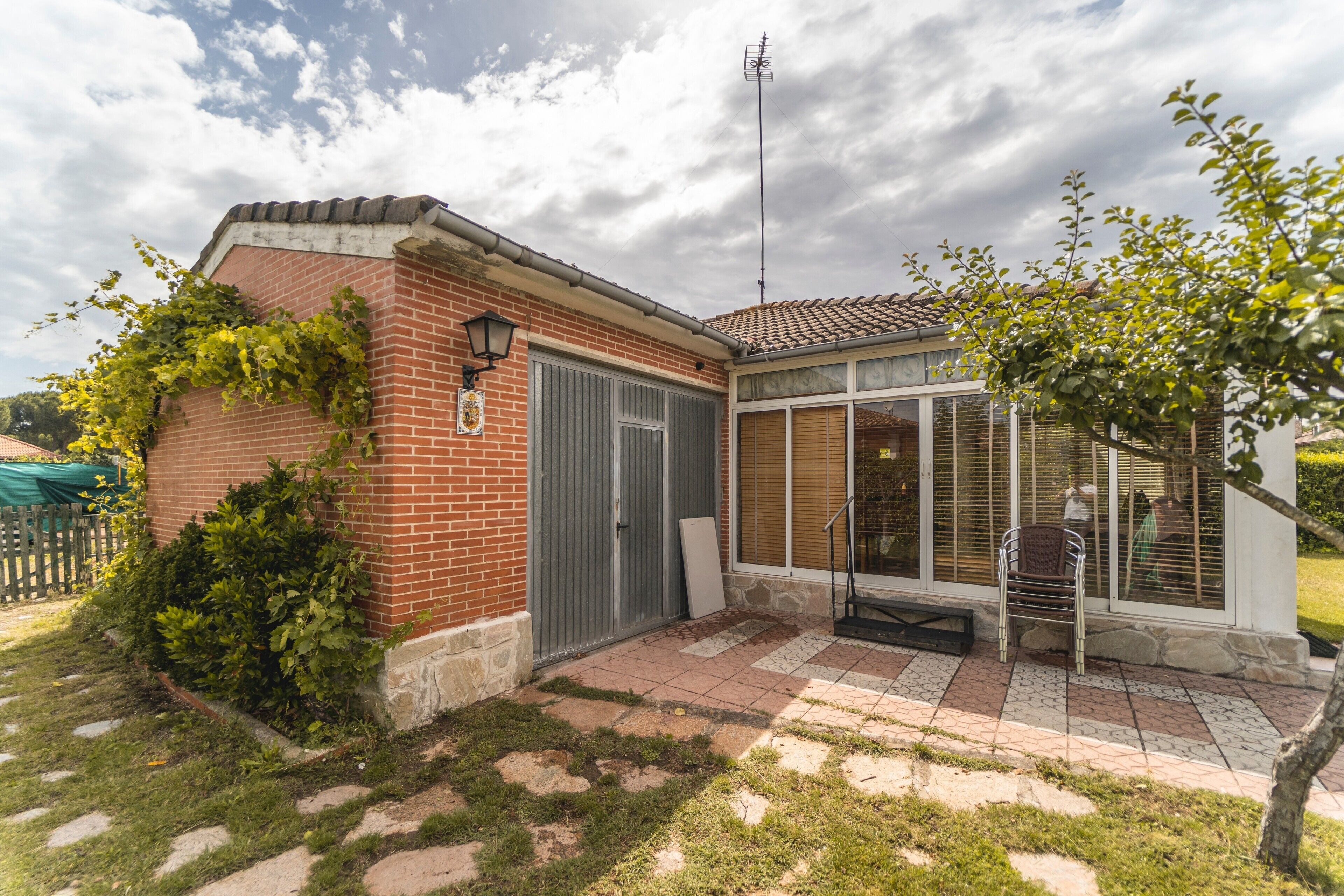 Una casa de ladrillo con un porche cubierto, una reja de metal y un pequeño jardín.