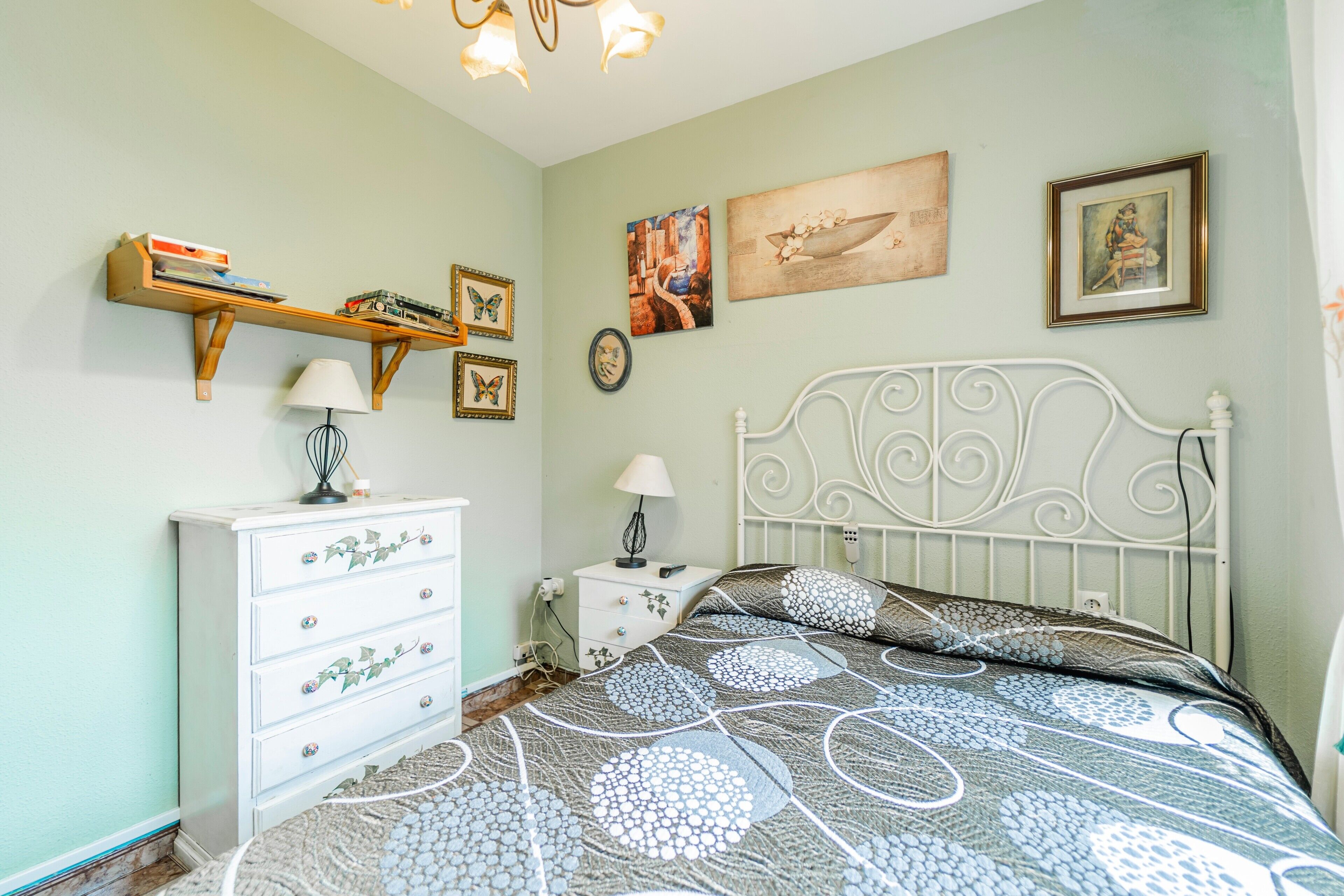 A bedroom with a bed, a dresser, a nightstand, a lamp, and wall art.