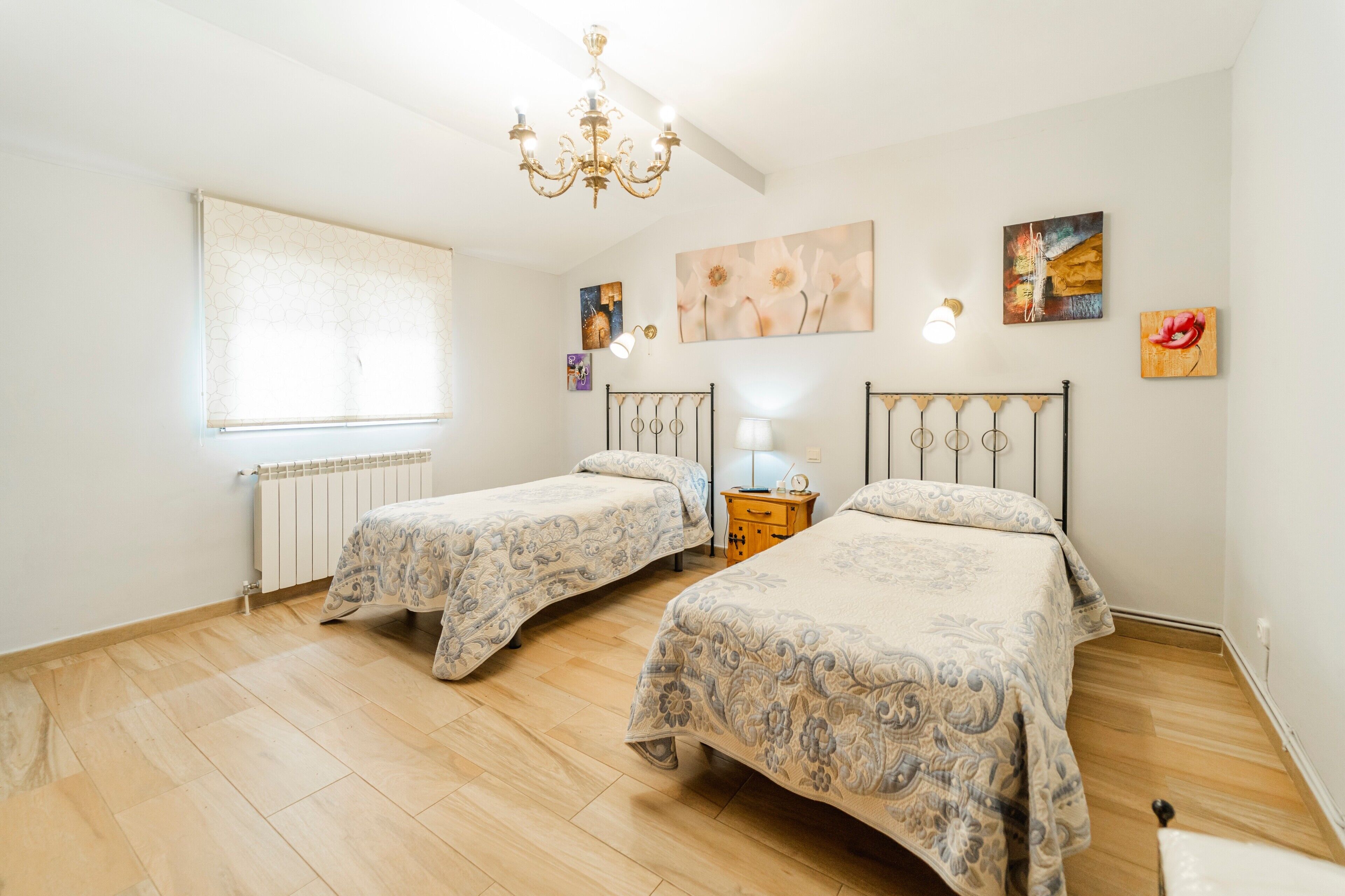 Una camera da letto con due letti, un lampadario, un termosifone e opere d'arte alle pareti.