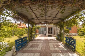 Un espace extérieur abrité, doté d’un sol carrelé, de bancs et d’une entrée de bâtiment.