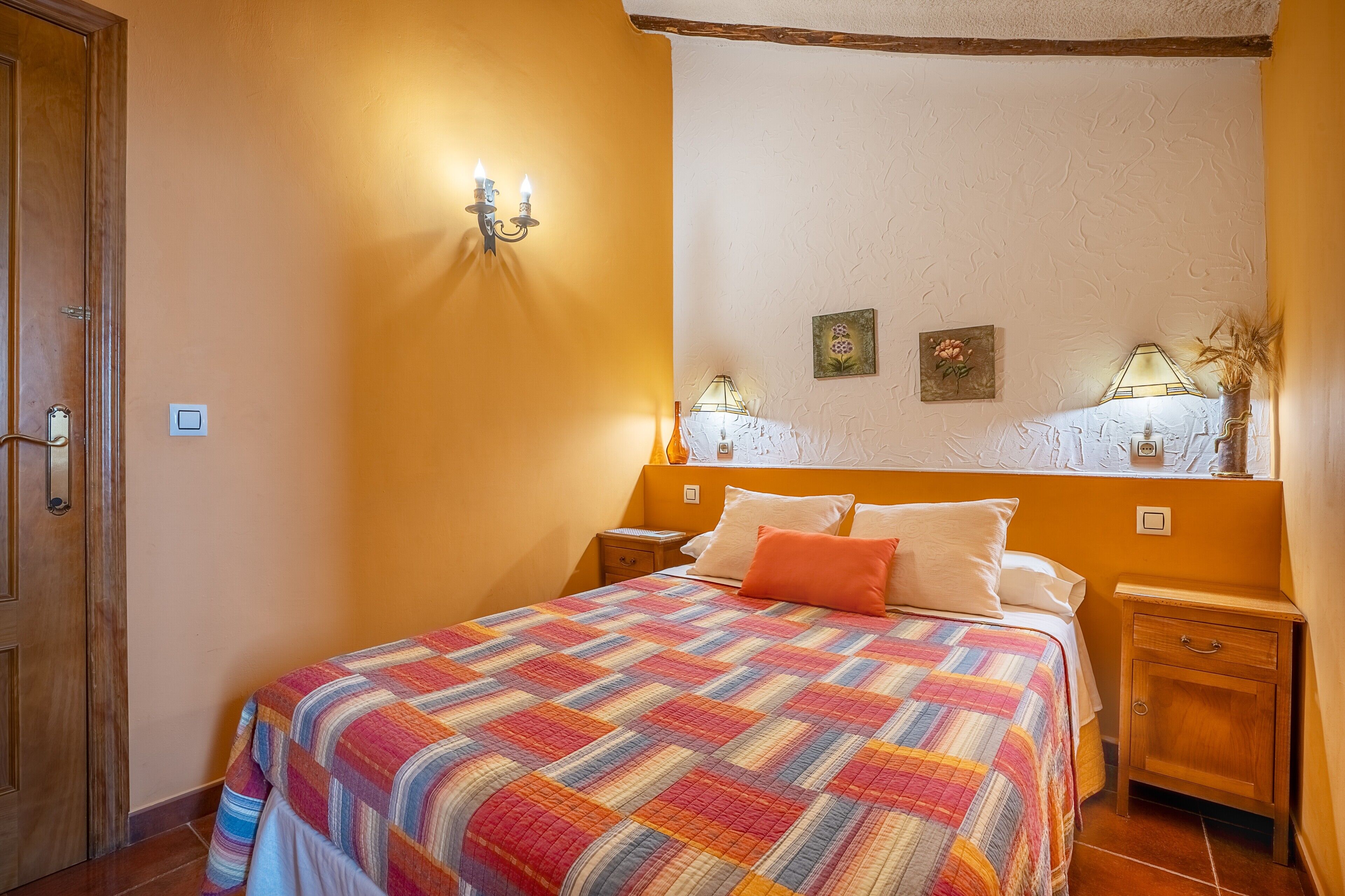 A bedroom with a bed, two bedside tables, a wall-mounted lamp, and a door.