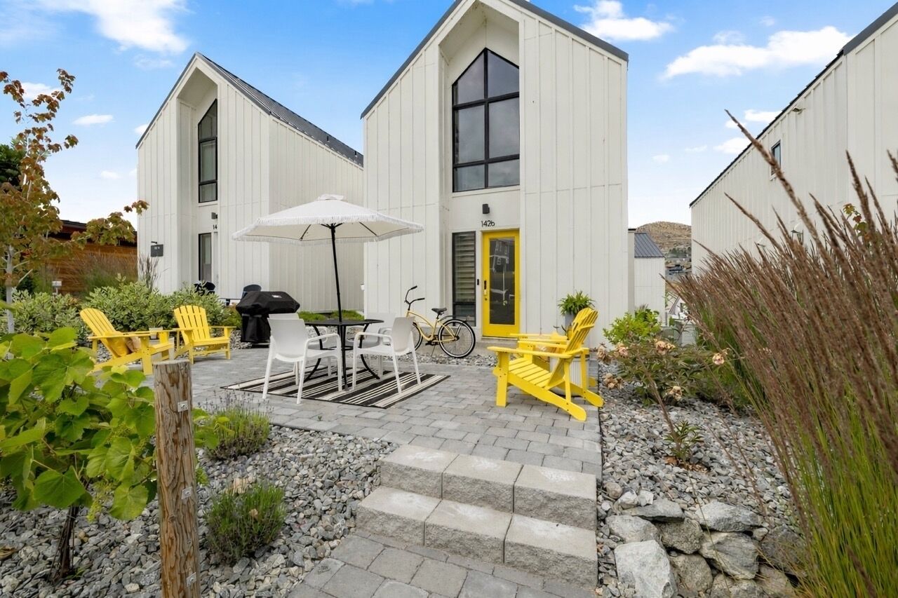 A building with a gabled roof, a yellow door, and a patio area with outdoor seating and a bicycle.