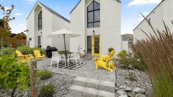 A building with a gabled roof, a yellow door, and a patio area with outdoor seating and a bicycle.