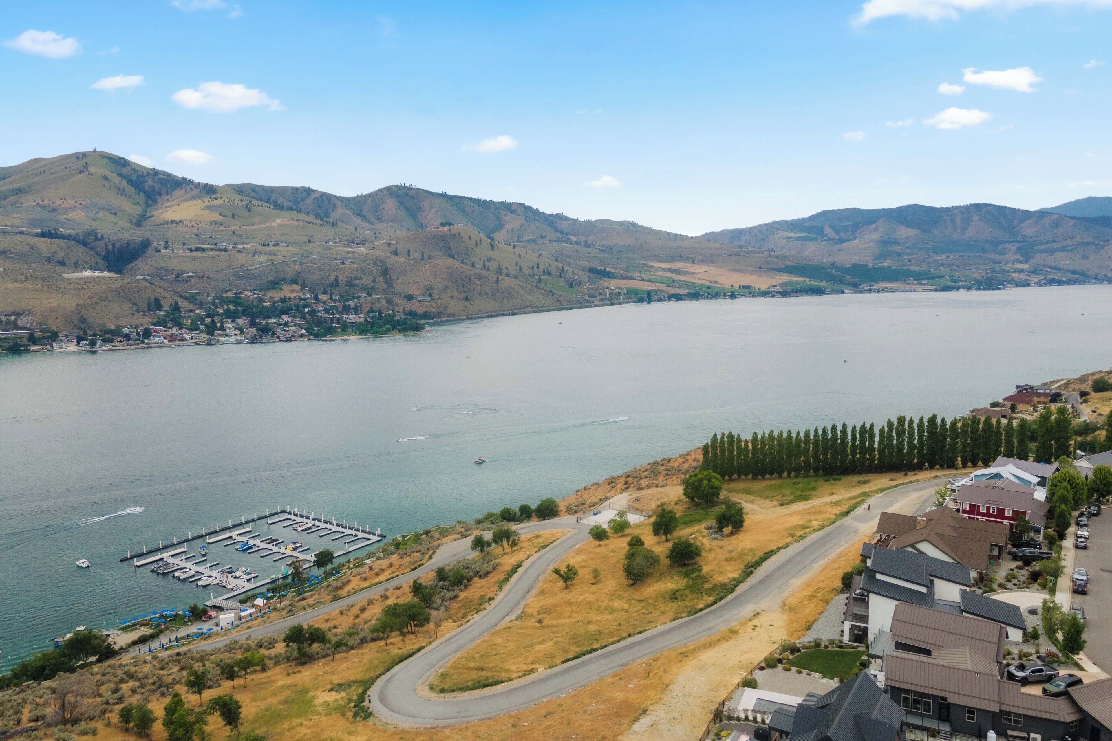 A coastal town with a marina, residential buildings, and hilly terrain in the background.