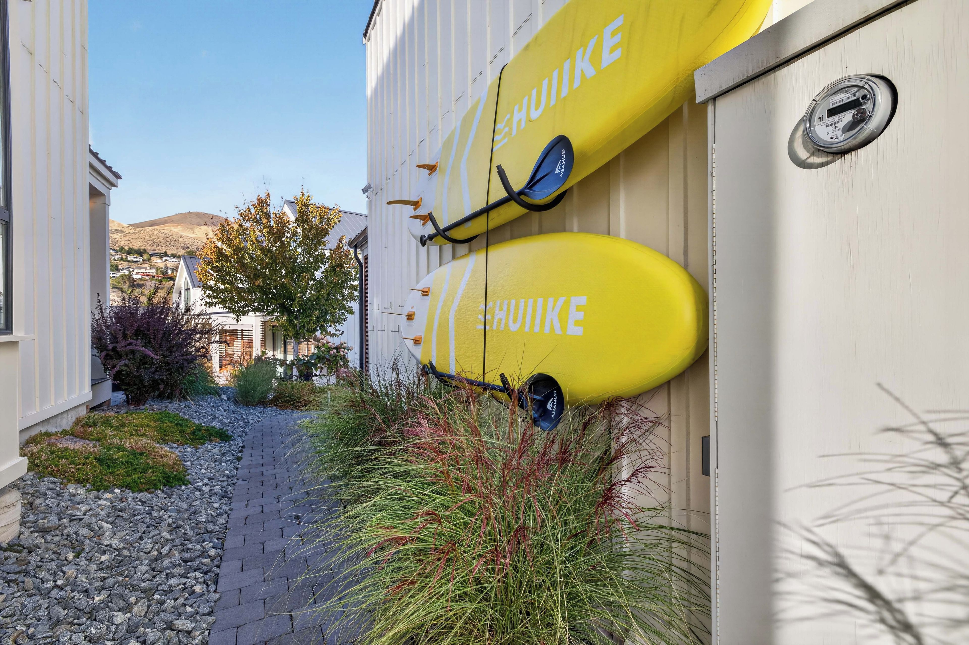 A building with two yellow surfboards mounted on the wall, a paved pathway, and a hillside in the background.