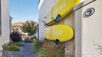 A building with two yellow surfboards mounted on the wall, a paved pathway, and a hillside in the background.