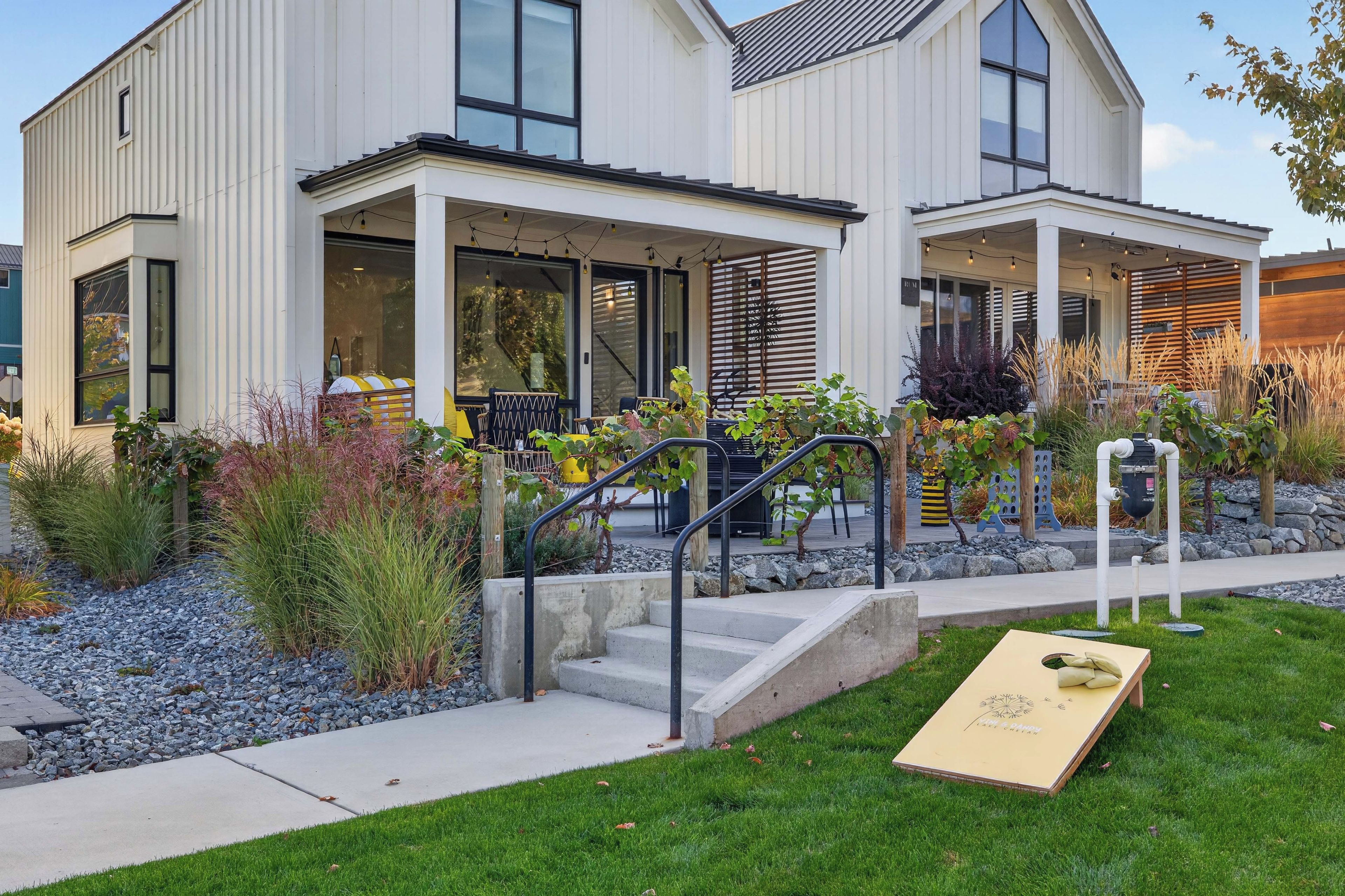 A modern two-story house with a covered porch, outdoor seating, and a well-maintained garden.