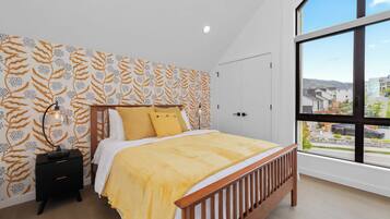 A bedroom with a large window, a bed with a wooden headboard, and patterned wallpaper.