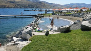 Een vakantiecomplex aan het meer met een zwembadgedeelte omringd door rotsen, een steiger en bergen op de achtergrond.