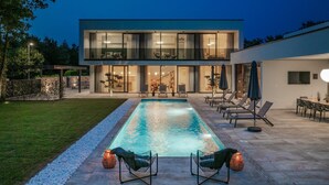 A modern two-story house with a swimming pool, outdoor seating, and a well-maintained garden.