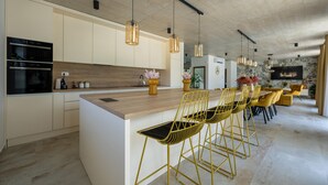 A modern kitchen with a large island, gold bar stools, pendant lighting, and a dining area with yellow chairs.