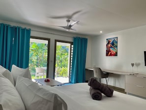 A hotel room with a bed, a desk, a chair, a ceiling fan, and a view of the outdoors. - Mareta Lodge (Bora Bora)