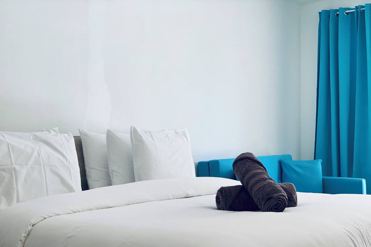 A neatly made bed with white bedding and a rolled-up towel.