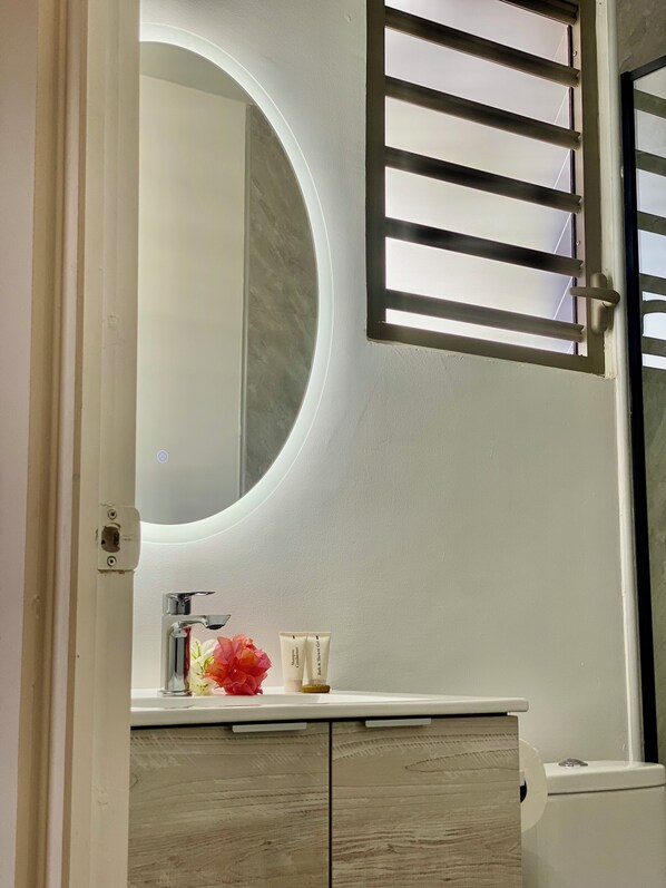 A bathroom with a round mirror, a toilet, and a sink. - Mareta Lodge (Bora Bora)