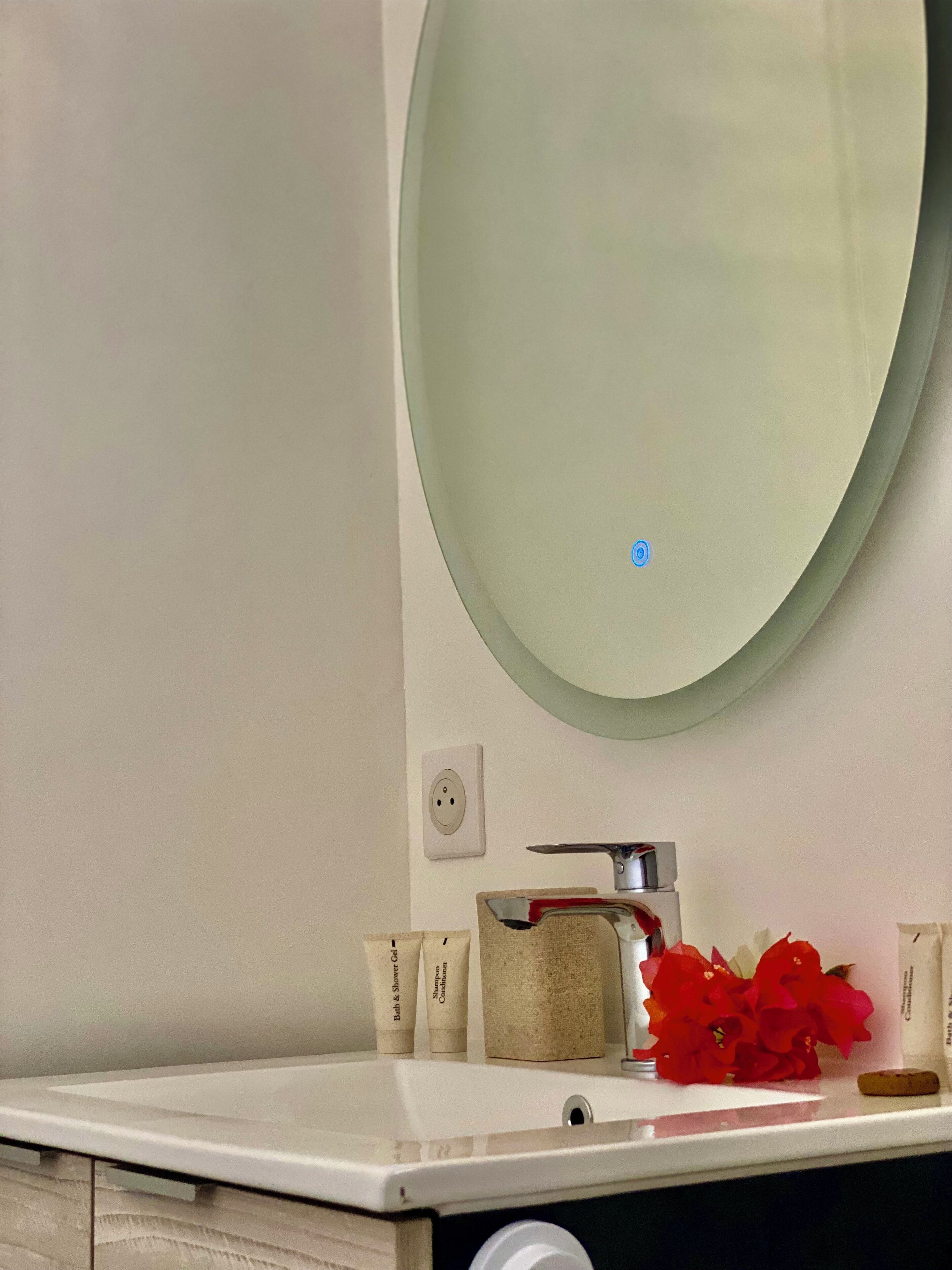 A bathroom with a white sink, a round mirror, and toiletries on the counter.