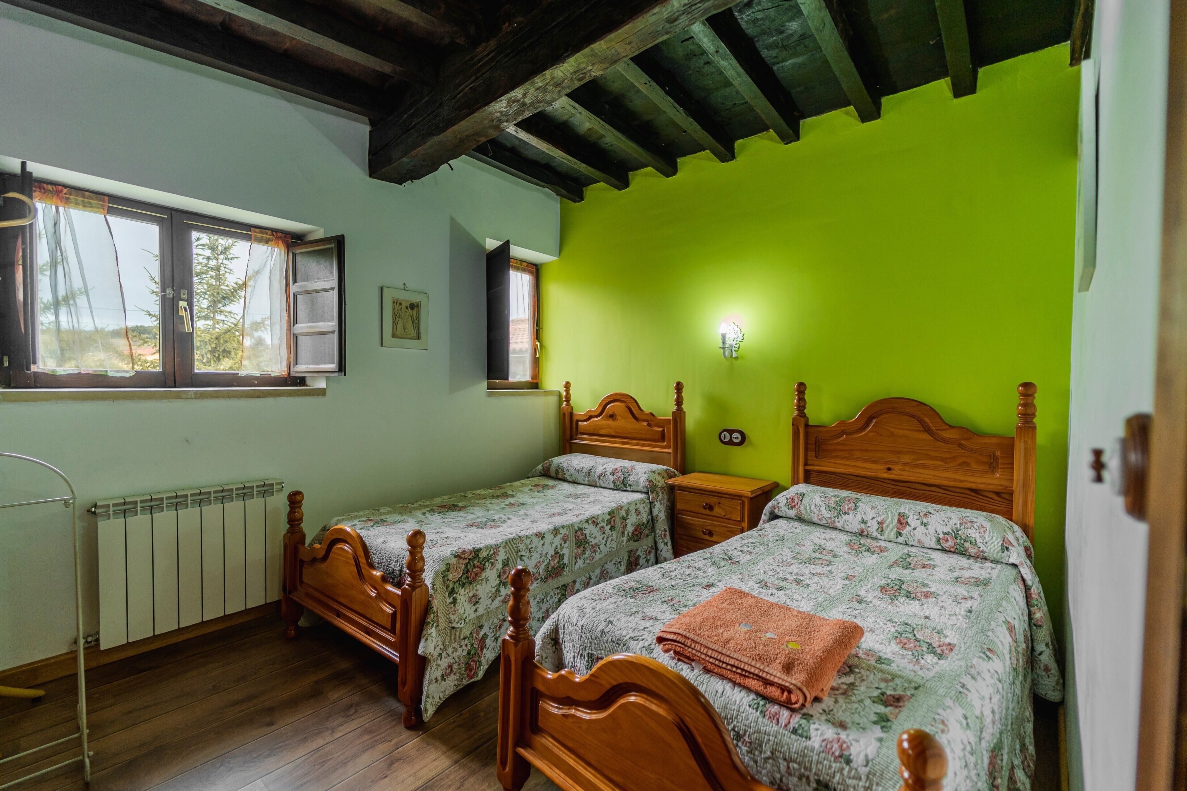 Un dormitorio con dos camas de madera, un radiador, una ventana y una pared verde.