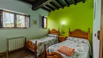Un dormitorio con dos camas de madera, un radiador, una ventana y una pared verde.