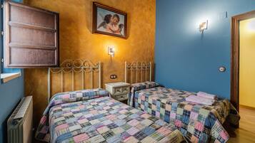 Una habitación con dos camas, cabecero de madera, un cuadro colgado en la pared, una mesita de noche y un radiador.