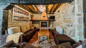 A rustic interior with stone walls, wooden beams, a fireplace, leather sofas, and a patterned rug.