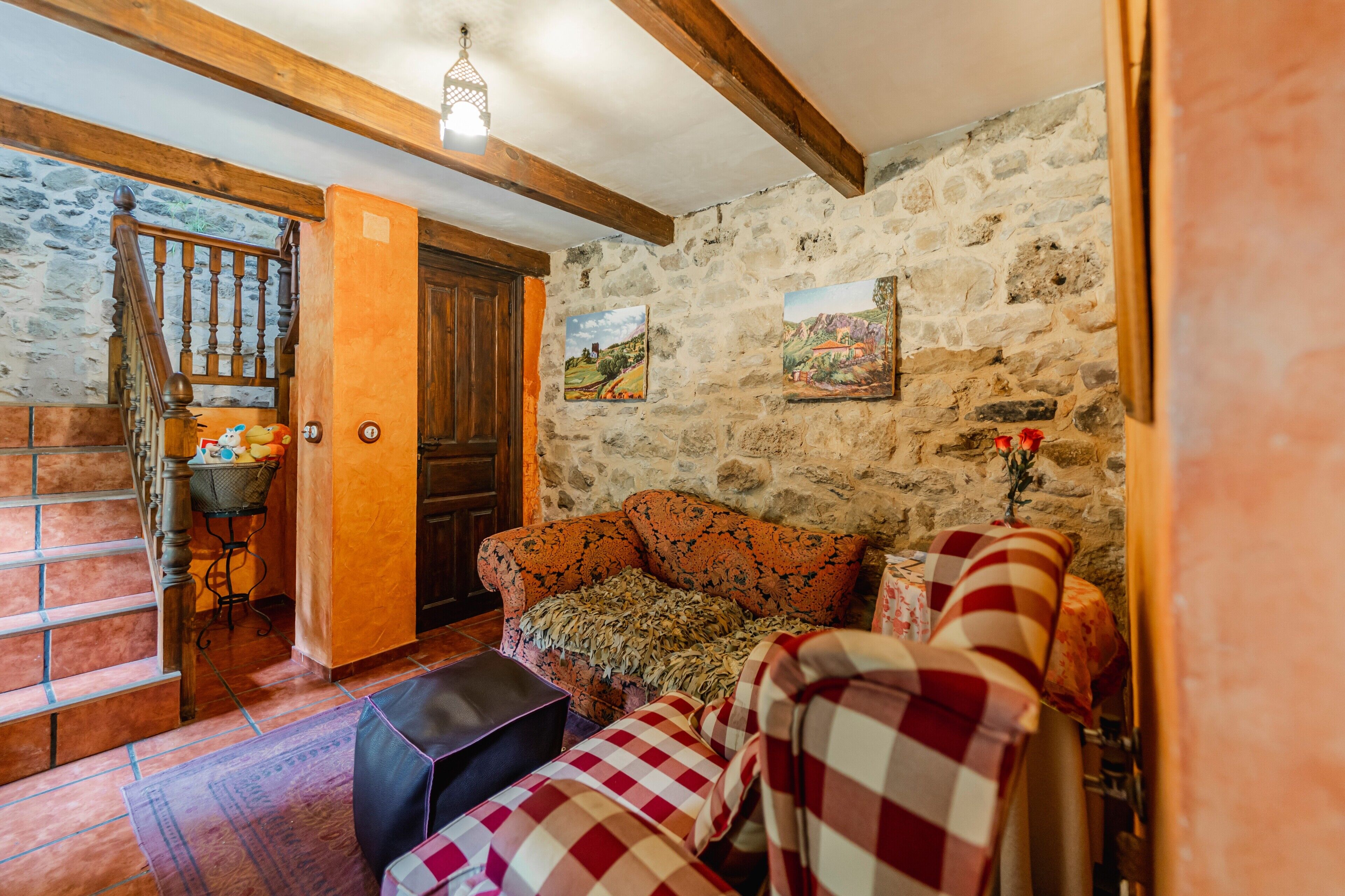 Un interno rustico con parete in pietra, scala in legno e un divano a fantasia.