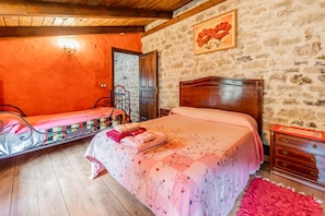 A bedroom with two beds, a wooden ceiling, a stone wall, and a wooden dresser.