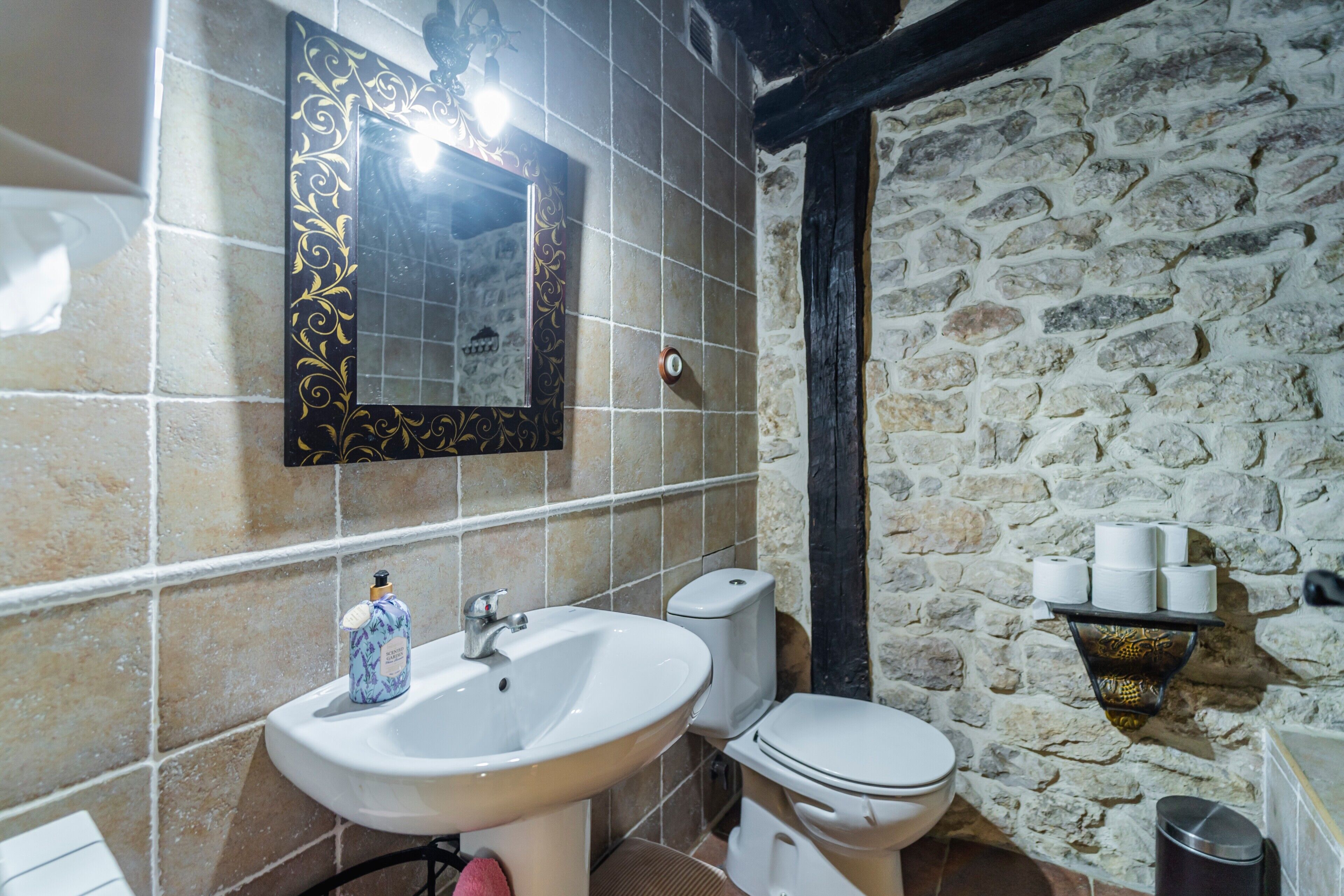 Een badkamer met een stenen muur, een witte wastafel, een toilet en een spiegel met een decoratieve lijst.