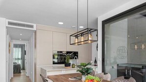 A modern kitchen with white cabinets, a wooden dining table, and a hanging light fixture. - Apartment 'Penthouse Santa Rosalia' with Private Pool, Wi-Fi and Air Conditioning (Santa Rosalia Torre Pacheco)