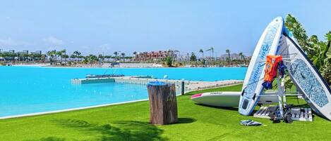 A poolside area with artificial grass, a wooden stump, and a surfboard leaning against a structure.