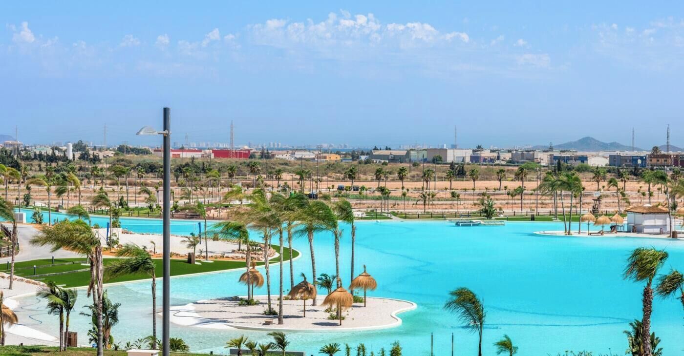 A resort with a large pool, palm trees, and a view of the city in the background.