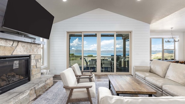 A spacious living room with a stone fireplace, a large TV, and a view of the ocean through sliding glass doors. - Private Beach Access! Tennis/Pickleball Courts Nearby! Game Room! (Fish Haven)