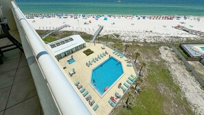 Et poolområde med liggestole, en swimmingpool og udsigt til strand og hav.