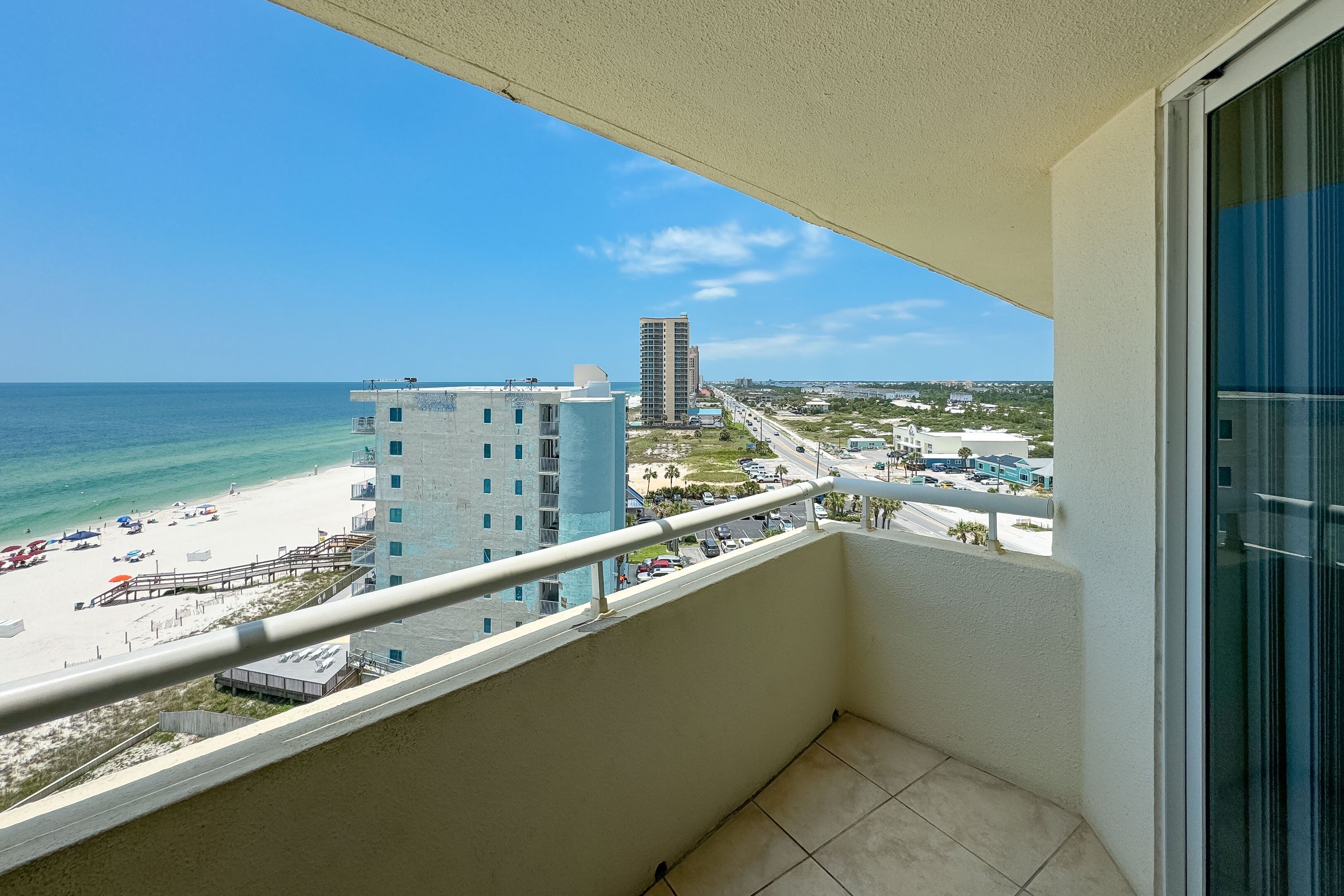Un balcón con vista a una playa, un edificio alto y una carretera.