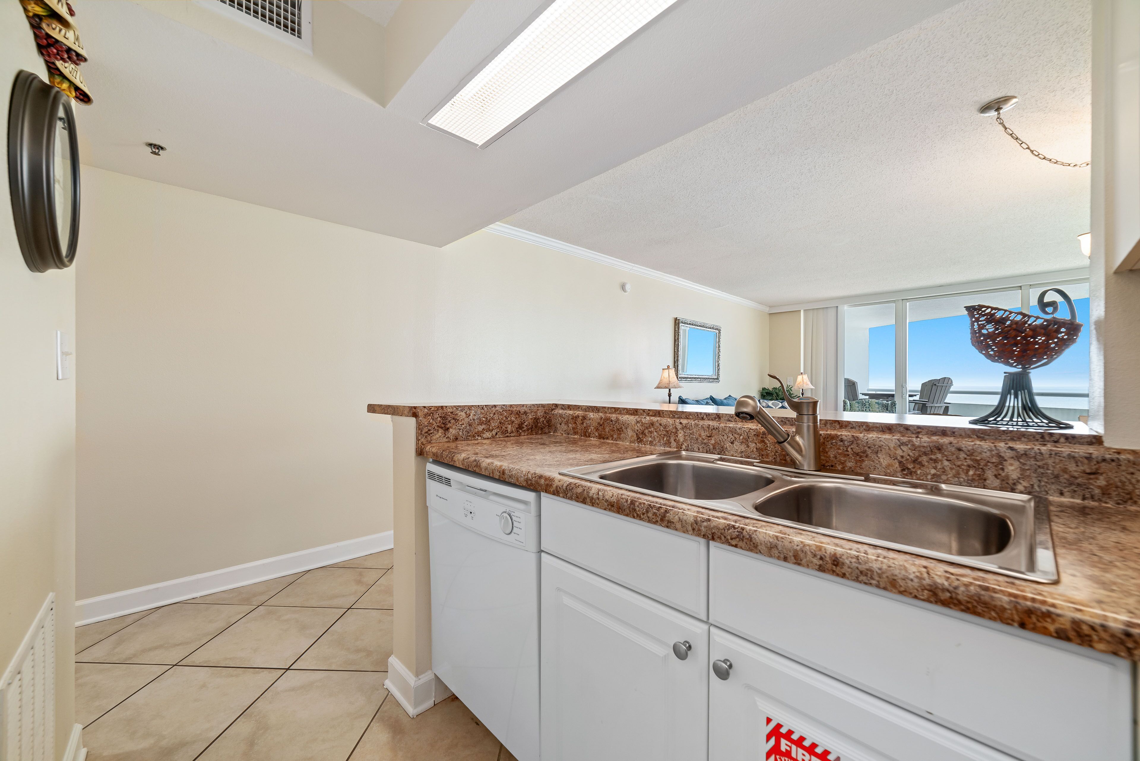 A kitchen with a double sink, granite countertop, white cabinets, and a view of the ocean through large windows.