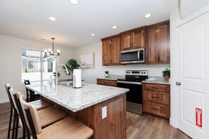 A modern kitchen with wooden cabinets, granite countertops, stainless steel appliances, and a bar area with seating.