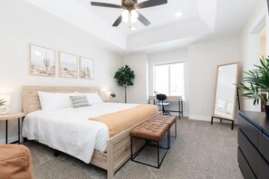 A bedroom with a bed, a bench, a desk, a mirror, and a ceiling fan.