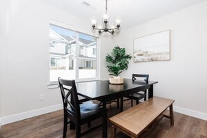 A dining room with a large table, chairs, a bench, a chandelier, a potted plant, and a framed picture on the wall.
