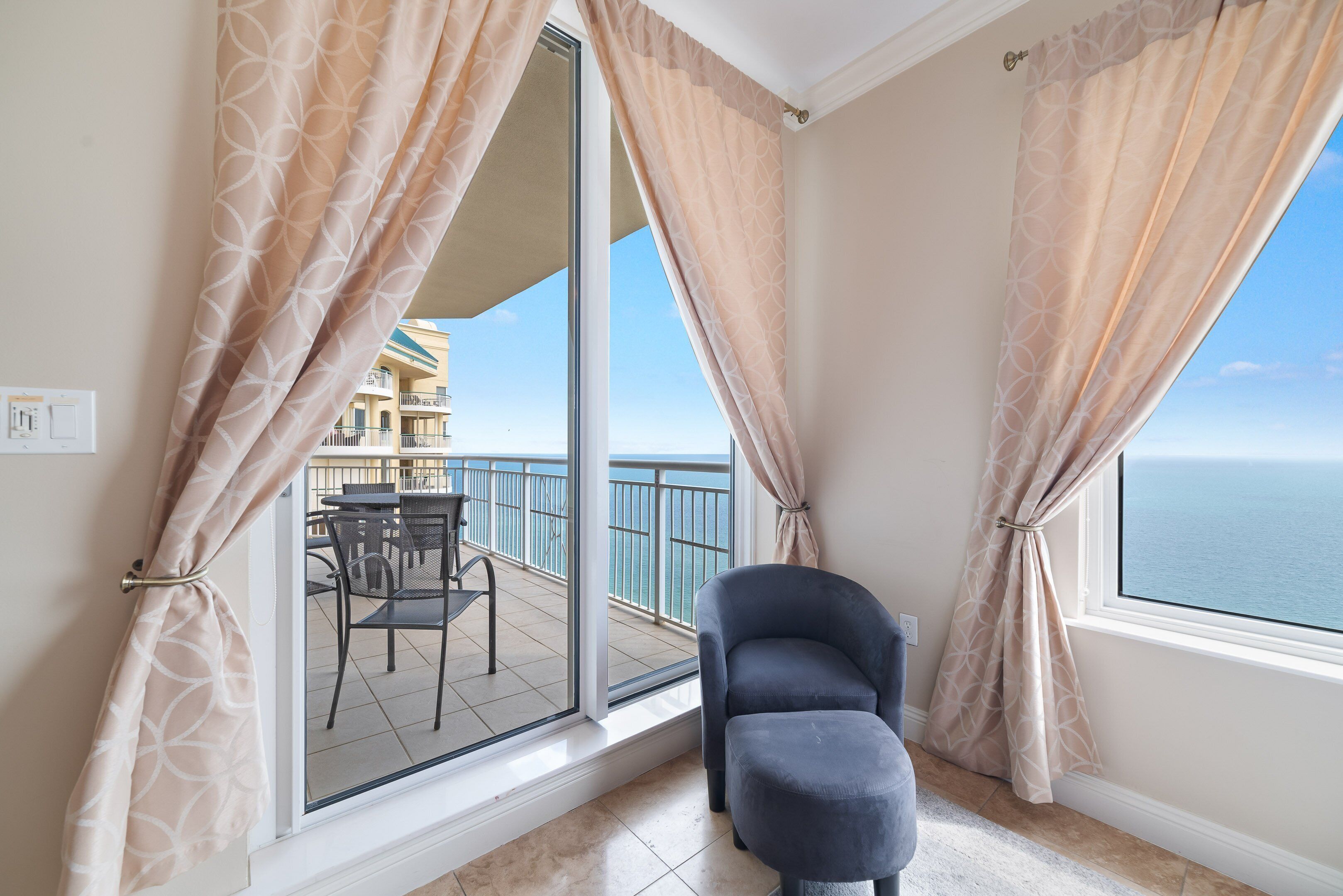 Un balcón con vista al mar, una silla y cortinas.