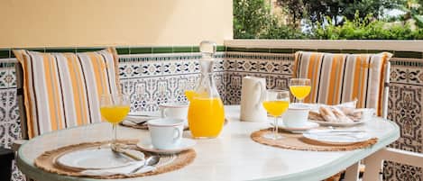 A round glass table with a white tablecloth, surrounded by striped cushions and a patterned tile wall.